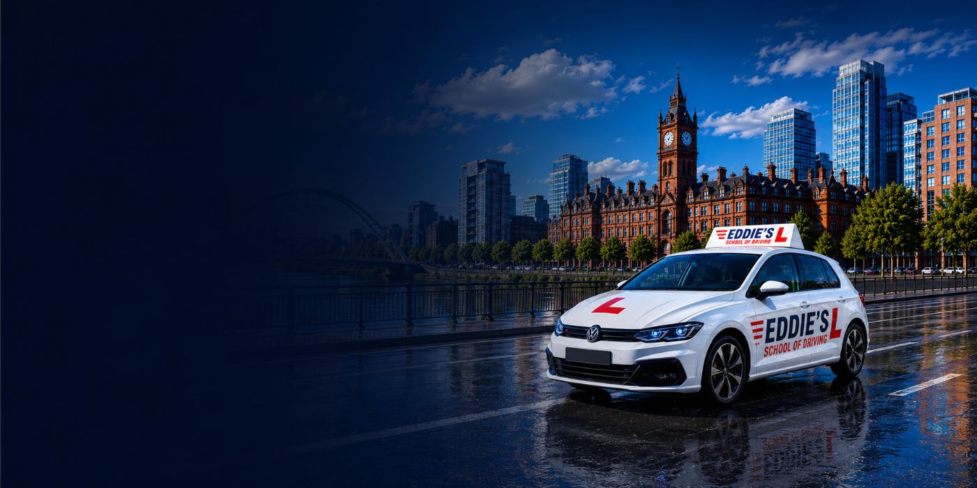Eddie's School of Driving car, in its red and navy livery with an L-plate on the roof, on a road beside the water in Manchester.