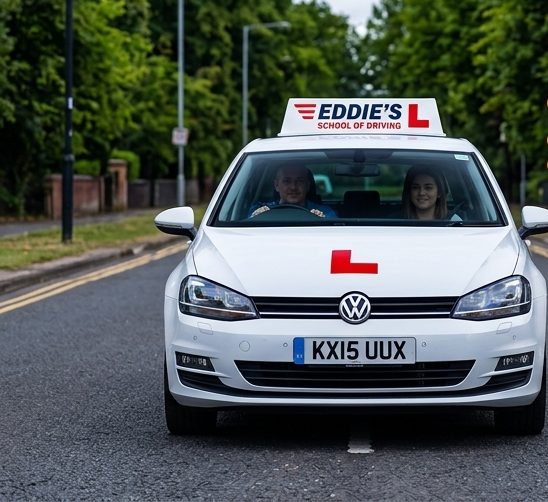 An Eddie's School of Driving car on a tree-lined road, an instructor in the passenger seat and a learner at the wheel.